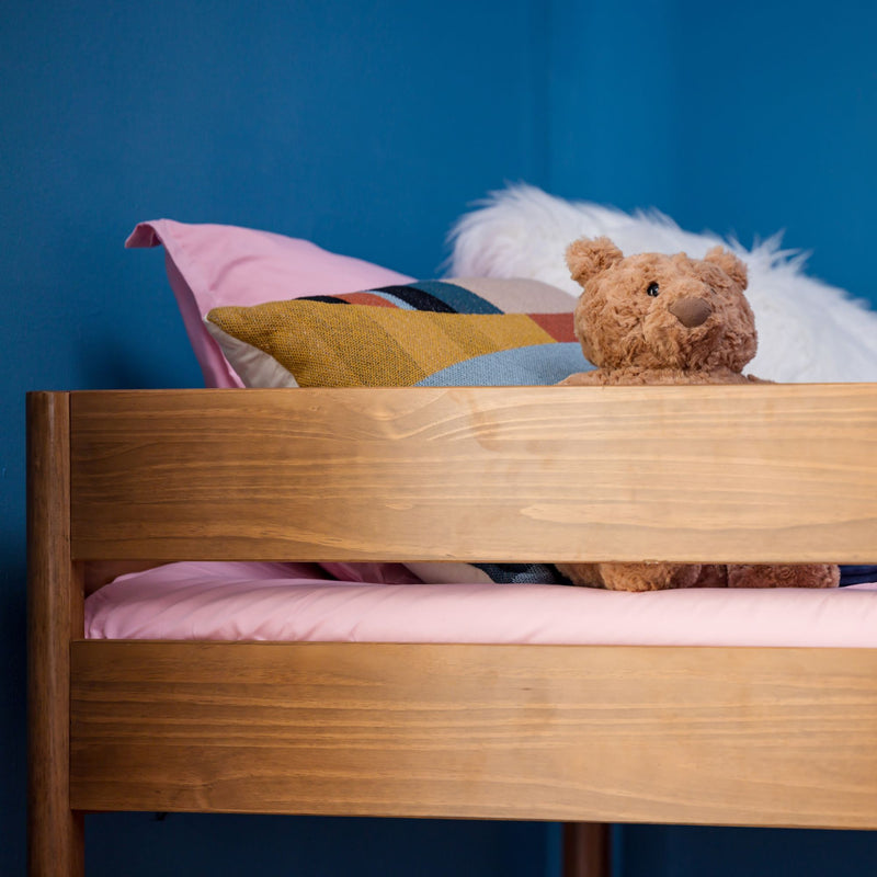 Wooden bunk bed with pink sheets, colorful geometric throw pillow and plush teddy bear in a blue children's bedroom