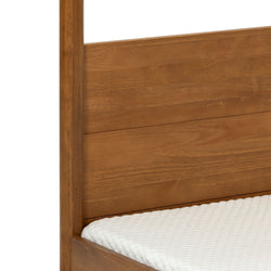 Close-up of solid wood bed frame with honey-toned panel headboard and side rail paired with a white quilted mattress topper