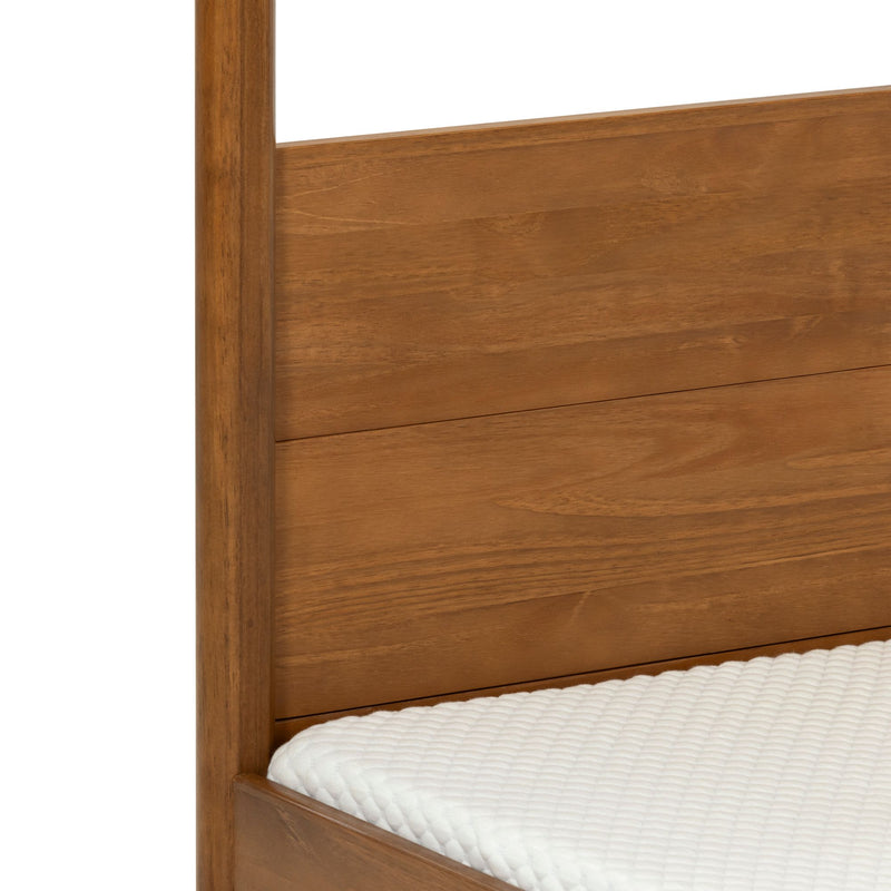 Close-up of warm brown solid wood bed frame and plank headboard showing wood grain and round post beside a white quilted mattress cover