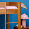 Wooden loft bed ladder and frame with pink bedding and lamp against blue wall in modern kids' bedroom — space-saving bunk bed