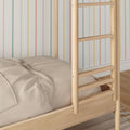 Close-up of natural wood bunk bed ladder and beige quilted bedding against pastel rainbow-striped wallpaper in a cozy children's bedroom.
