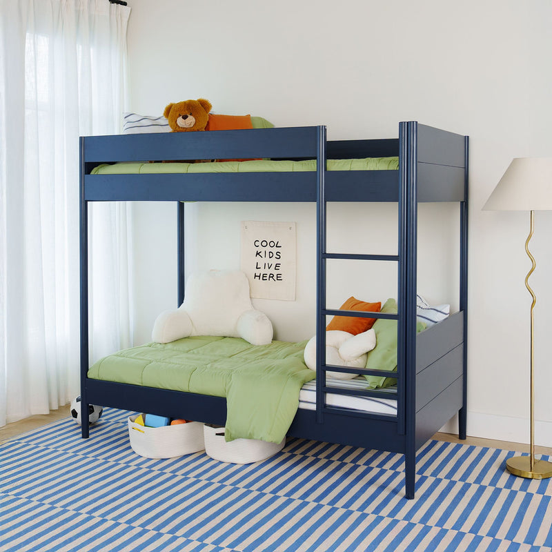 Modern kids bedroom with navy blue bunk bed and green bedding, teddy bear on top, plush chair, "Cool Kids Live Here" wall sign and blue striped rug