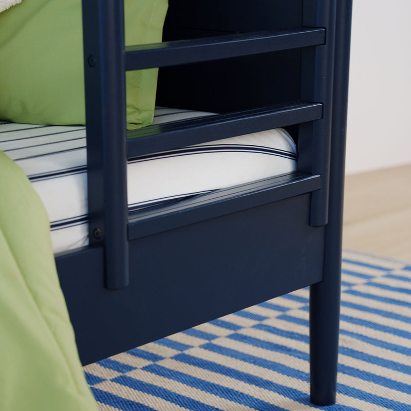 Close-up of navy blue wooden bed frame with white-and-navy striped mattress, green bedding and blue-striped rug in a modern bedroom
