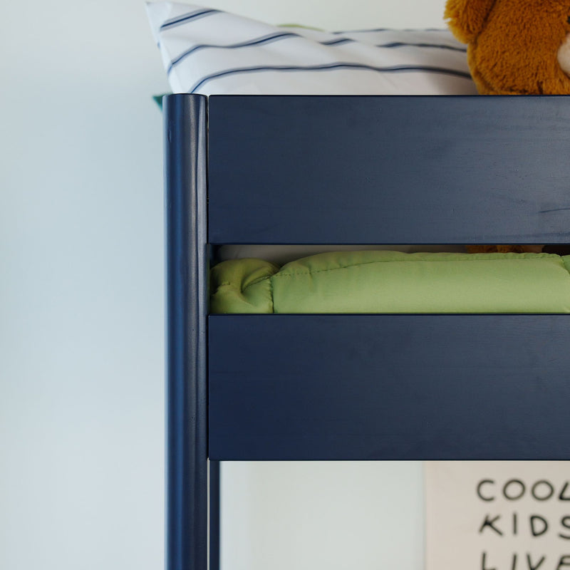 Navy blue wooden bunk bed top corner with green comforter, striped pillow and teddy bear in kids bedroom