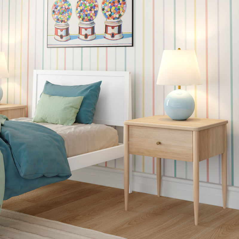 Cozy modern kids' bedroom with white twin bed, teal duvet and green throw pillow, natural wood nightstand with light blue ceramic table lamp, pastel striped wallpaper and colorful gumball machine wall art.