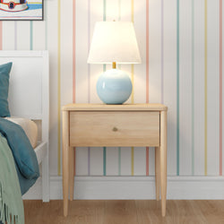 Modern Scandinavian wooden nightstand with blue ceramic table lamp on pastel striped wallpaper beside white bed with teal bedding