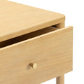 Light wood nightstand with partially open drawer, round brass knob and tapered legs in modern minimalist bedroom furniture style