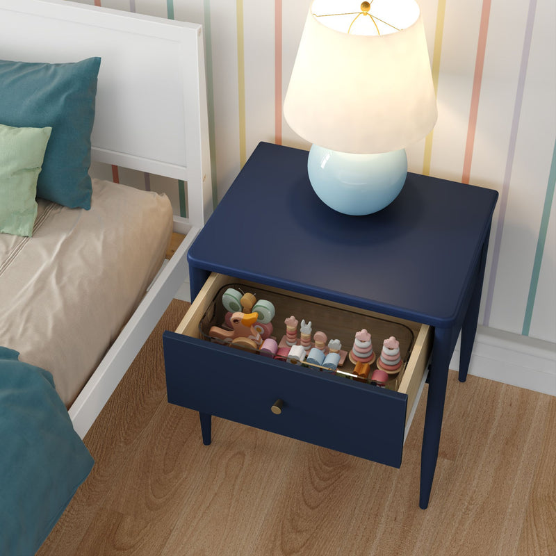 Navy blue nightstand with open drawer full of pastel wooden toys and a round blue table lamp beside a white bed in a children's bedroom with striped wallpaper and hardwood floor