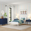 Bright modern kids bedroom with white twin bed, blue bedding, navy nightstands and dresser, pastel striped wallpaper, gumball print, large window