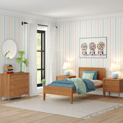 Bright modern kids bedroom with mid-century wooden bed and blue bedding, pastel striped wallpaper, gumball machine wall art, matching nightstands and dresser, white curtains, plant and neutral area rug.