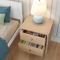 Light wood children's nightstand with blue lamp, two open drawers of toys and colorful children's books beside a white bed and striped wall