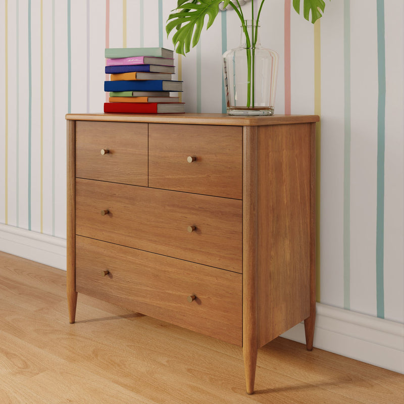Mid-century modern wooden dresser with four drawers, stack of colorful books and glass vase holding monstera leaves on top, light hardwood floor and pastel striped wallpaper
