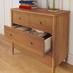 Mid-century modern wooden dresser with open drawer showing folded linens, brass knobs, books and glass vase on hardwood floor