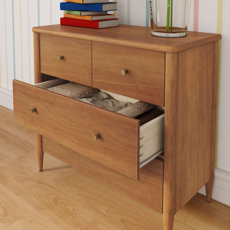 Mid-century modern wooden dresser with open drawer showing folded linens, brass knobs, books and glass vase on hardwood floor