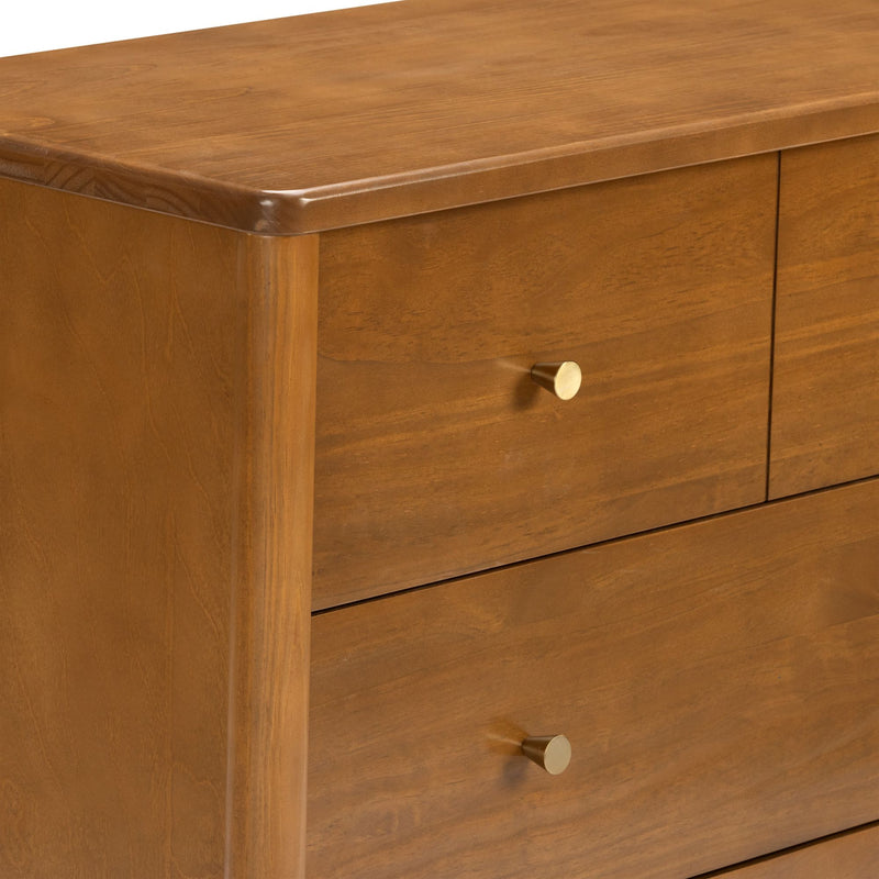 Close-up of a mid-century modern wooden dresser with warm walnut finish, rounded top edge and brass drawer knobs