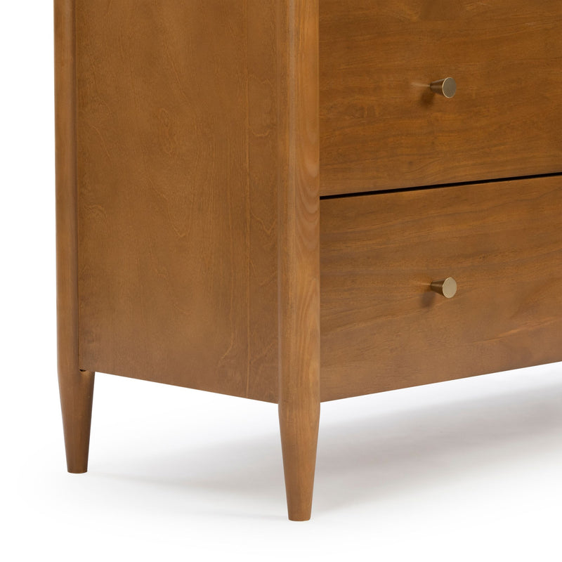 Close-up of a mid-century modern walnut dresser corner with tapered legs, warm wood grain finish and round brass drawer knobs