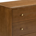 Close-up of a mid-century modern honey-brown wooden dresser with smooth wood grain, round brass knobs and stacked drawers for bedroom storage