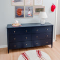 Navy blue six-drawer dresser in kids' sports-themed bedroom with white table lamp, baseball rug, stacked children's books and framed sports wall art