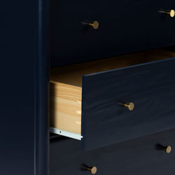 Navy blue wooden dresser with an open drawer revealing natural pine interior and brass knobs, modern bedroom storage chest
