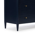 Close-up of navy blue mid-century modern wooden dresser corner with tapered legs and brass knobs