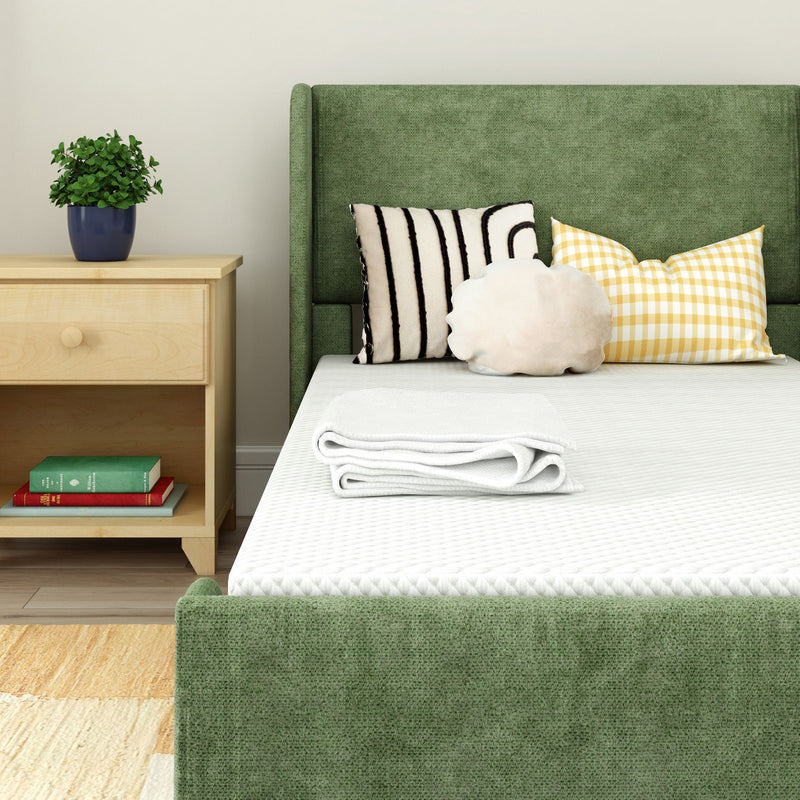 Cozy modern bedroom with green upholstered bed, striped and checkered pillows, and wooden nightstand with books and a plant.