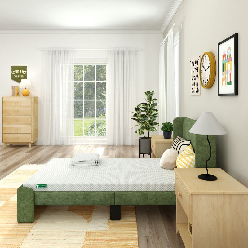 Bright minimalist bedroom with green upholstered bed, light wood nightstands and dresser, large window with sheer curtains, potted plant and wall art