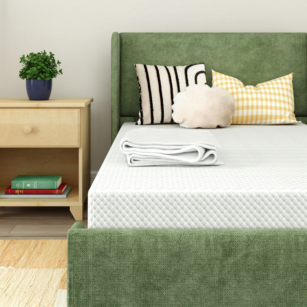 Green upholstered bed with patterned pillows and cozy blanket in modern bedroom setting.
