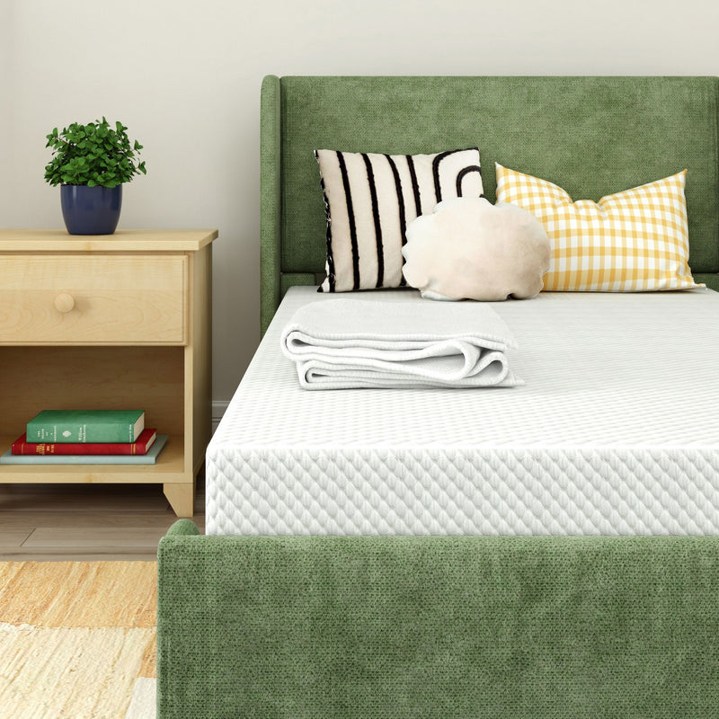 Green upholstered bed with white mattress and folded blanket, decorative pillows, wooden nightstand and potted plant in a modern cozy bedroom