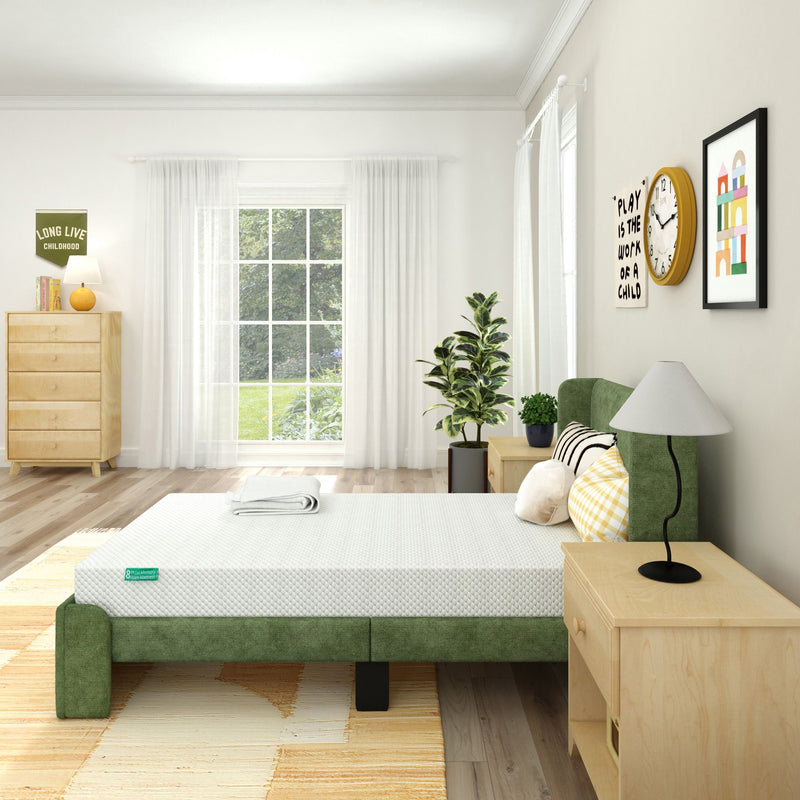 Bright modern bedroom with green upholstered bed and white mattress, natural wood nightstands and dresser, large window with sheer curtains, indoor plant and minimalist wall art