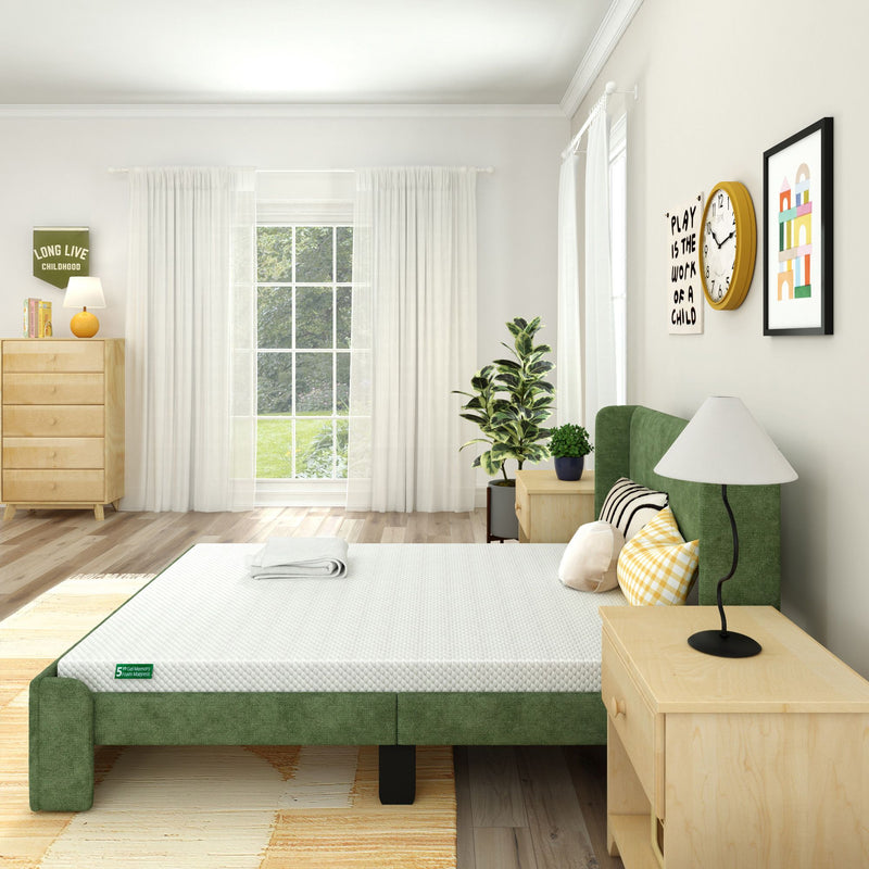 Modern bedroom with green upholstered bed, white mattress, wooden nightstand, indoor plant, and natural light from a large window.