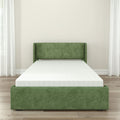 Green upholstered bed frame with white mattress in a minimalist modern bedroom on hardwood floors with sheer white curtains