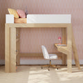 Modern children's wooden loft bed with built-in desk and ladder, white safety rail, pastel yellow and pink pillows and plush bunny, white swivel chair and pink desk lamp against pink geometric wallpaper