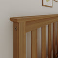 Close-up of a natural oak slatted wooden headboard bed frame against a white wall, highlighting the smooth top rail and wood grain