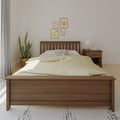 Minimalist bedroom interior with wooden bed frame, beige bedding, bedside table and lamp, potted plant and framed fruit wall art