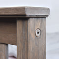 Close-up of rustic wooden furniture corner joint showing weathered gray-brown wood grain, vertical planks and exposed hex screw hardware