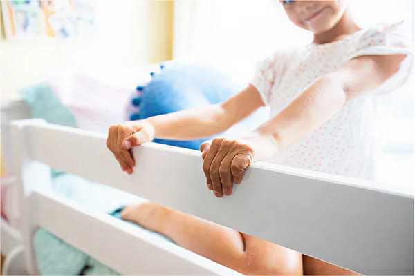 Child sitting on white bunk bed rail with decorative pillows in a bright bedroom.